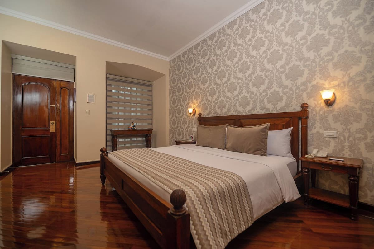A bedroom with a wooden bed, a nightstand with a lamp, and a door with a window blind.