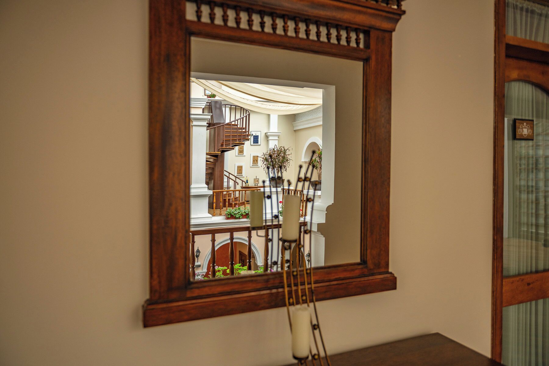 A mirror reflecting a staircase, a dining area with chairs, and potted plants.