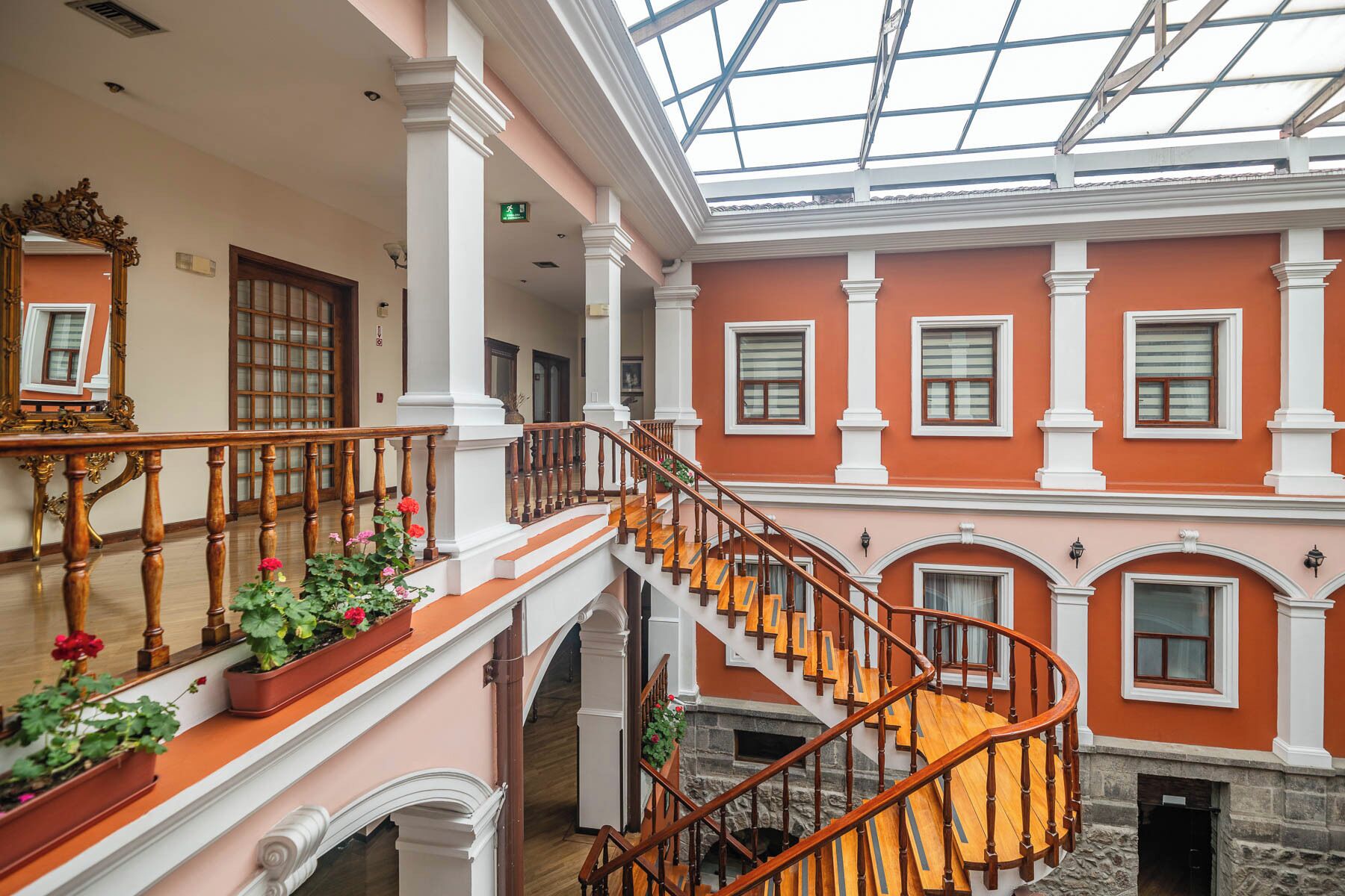 Un intérieur à plusieurs niveaux, doté d’un escalier en colimaçon central, de colonnes blanches et d’un plafond en verre.