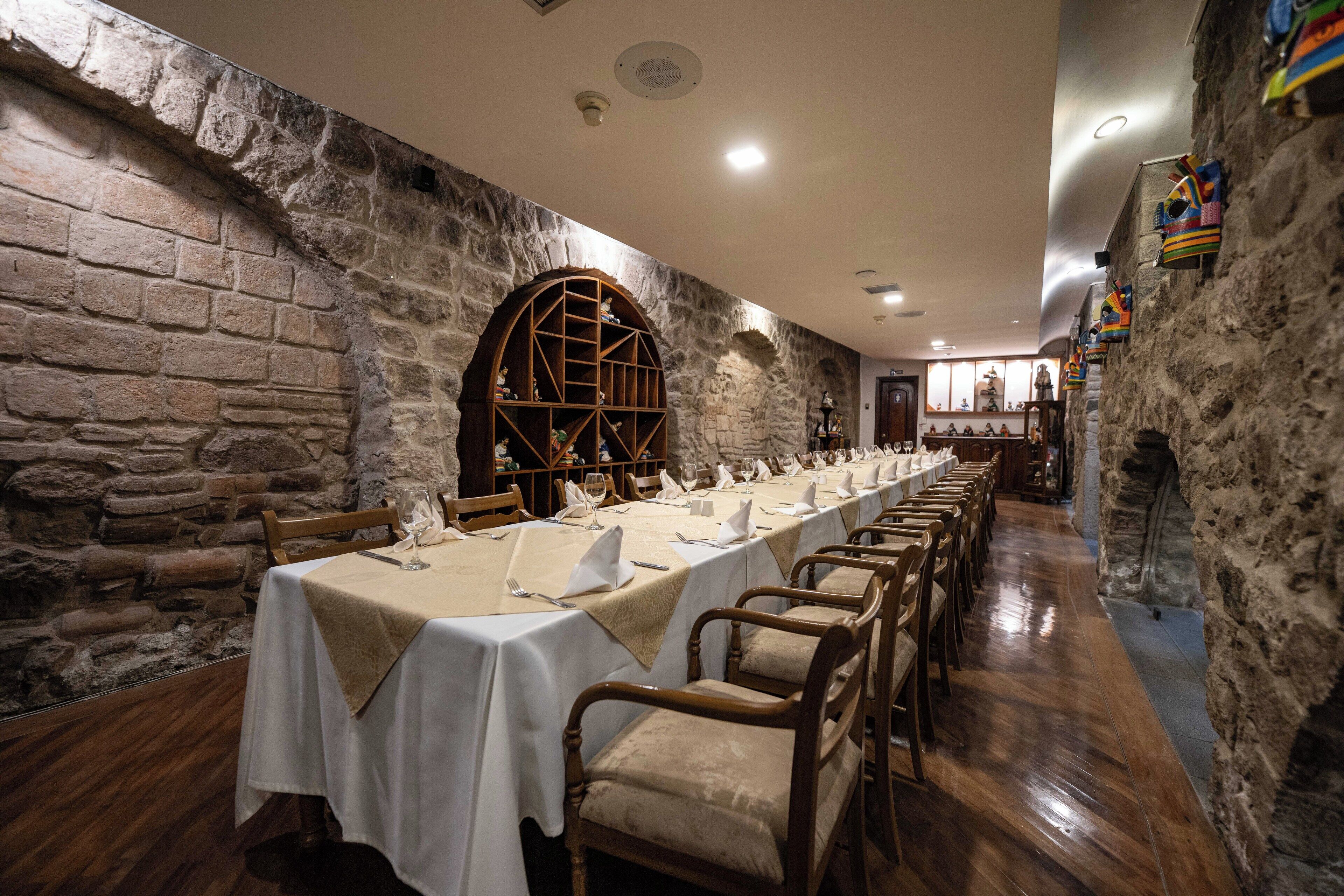 Una larga mesa de comedor con manteles blancos y sillas de madera en una sala con paredes de piedra.