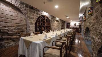 Una larga mesa de comedor con manteles blancos y sillas de madera en una sala con paredes de piedra.