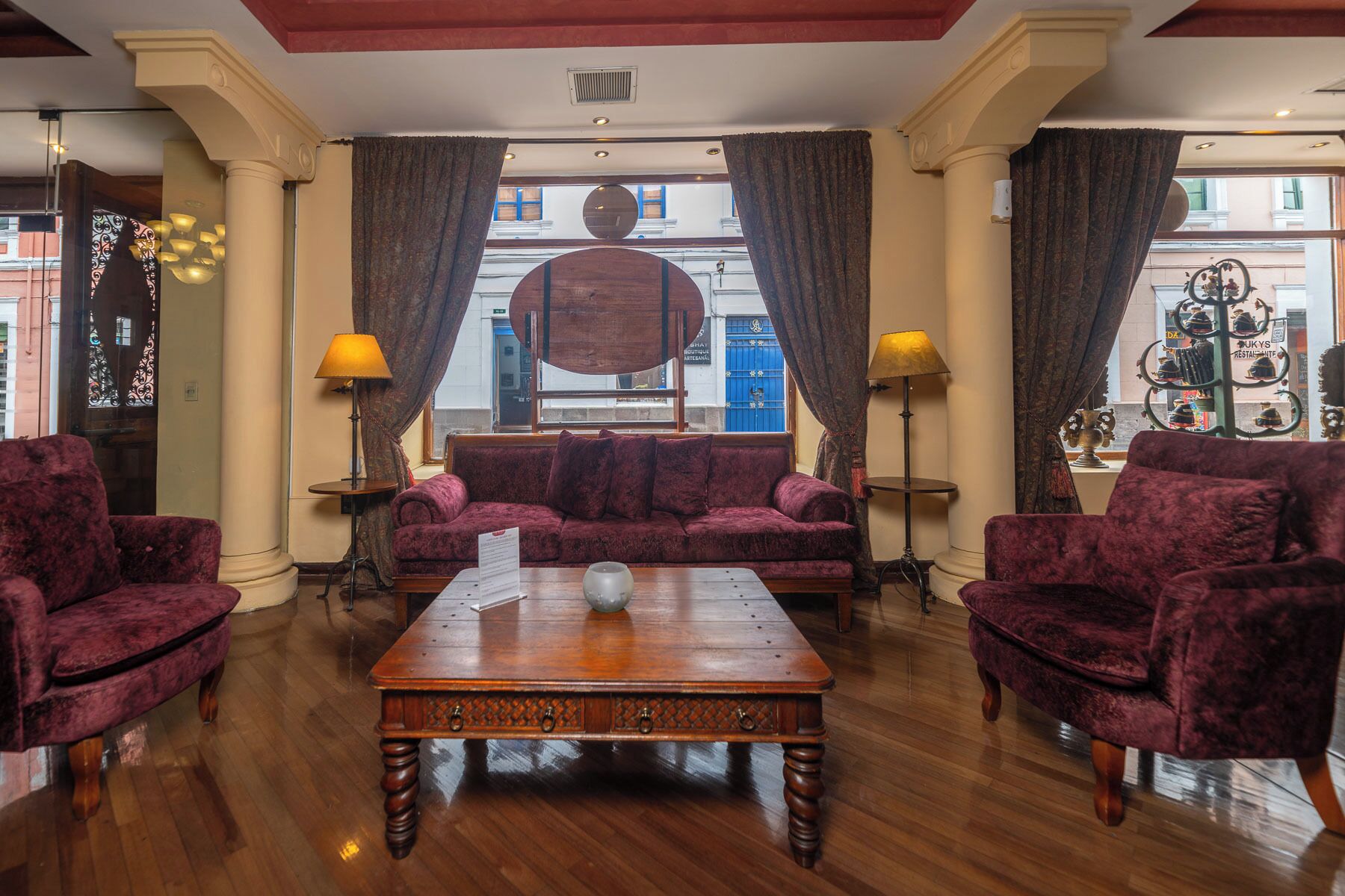 Un vestíbulo amplio con una mesa de centro de madera, cómodos sofás rojos y un gran ventanal con cortinas.