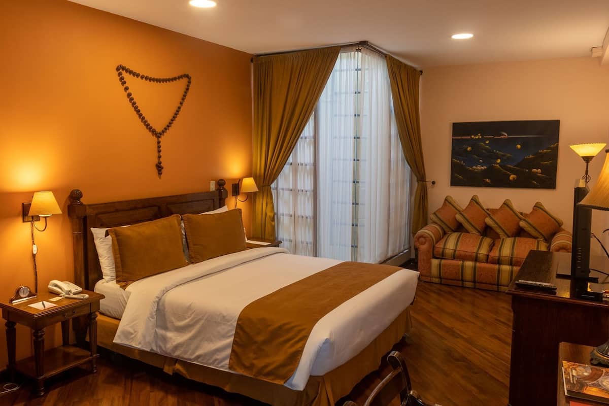 A hotel room with a bed, bedside lamps, a telephone, a painting, and a sofa.