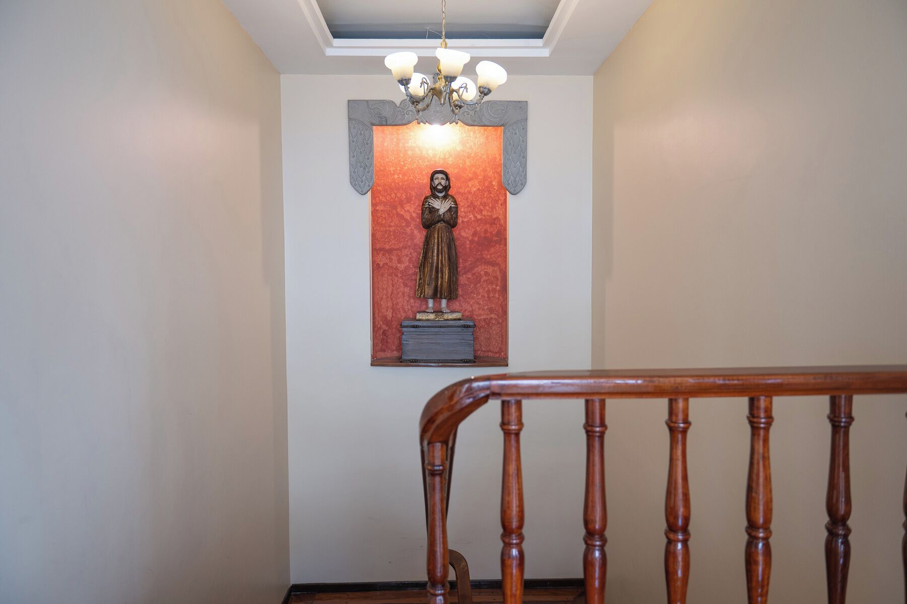 Una escalera con barandilla de madera que lleva a una habitación con una estatua en la pared.