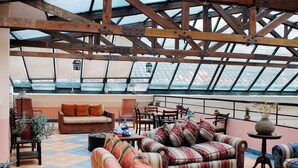 A spacious rooftop terrace with a wooden ceiling, furnished with sofas, chairs, and tables, featuring potted plants and a view of the cityscape. - Hotel Patio Andaluz (Quito)