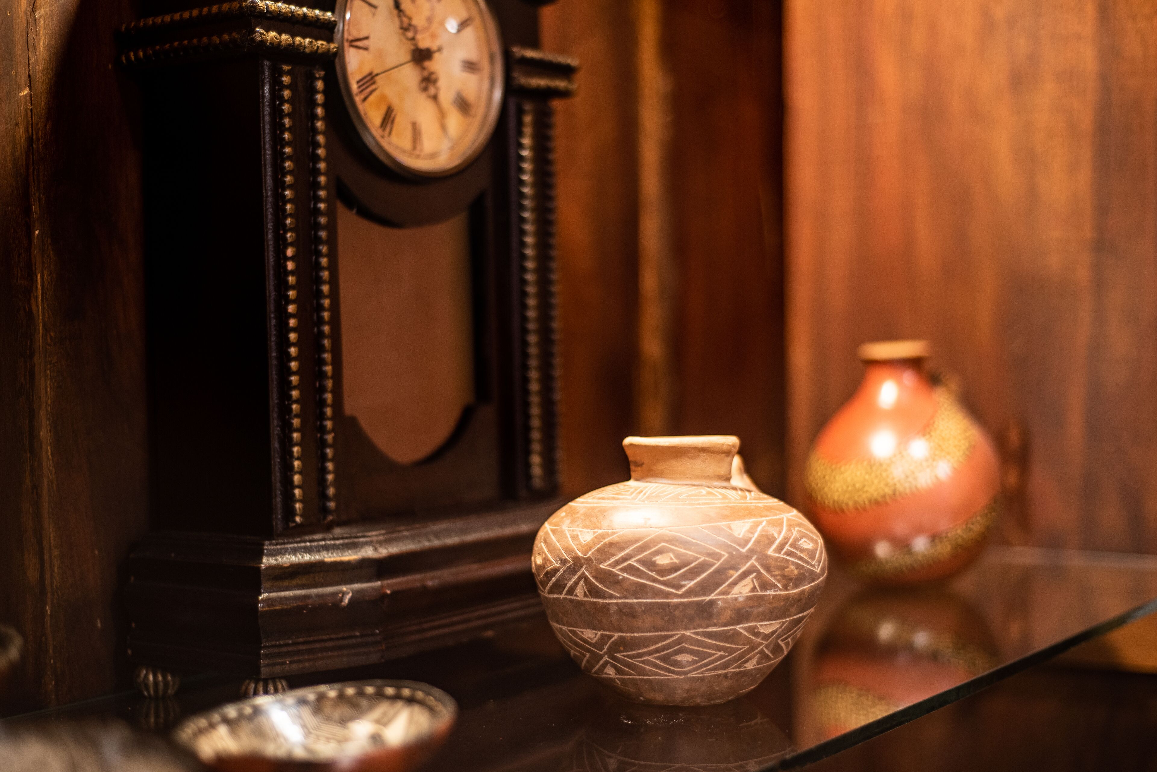 A clock, a vase, and a bowl on a reflective surface.