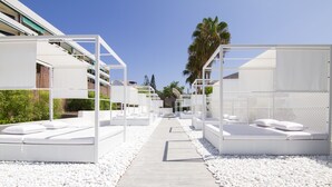 A pathway leading to white outdoor seating areas with cushions, surrounded by white pebbles, under a clear sky. - Checkin Bungalows Atlantida (Arona)