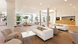 A spacious lobby with white sofas, patterned chairs, a reception desk, and large windows. - Checkin Bungalows Atlantida (Arona)