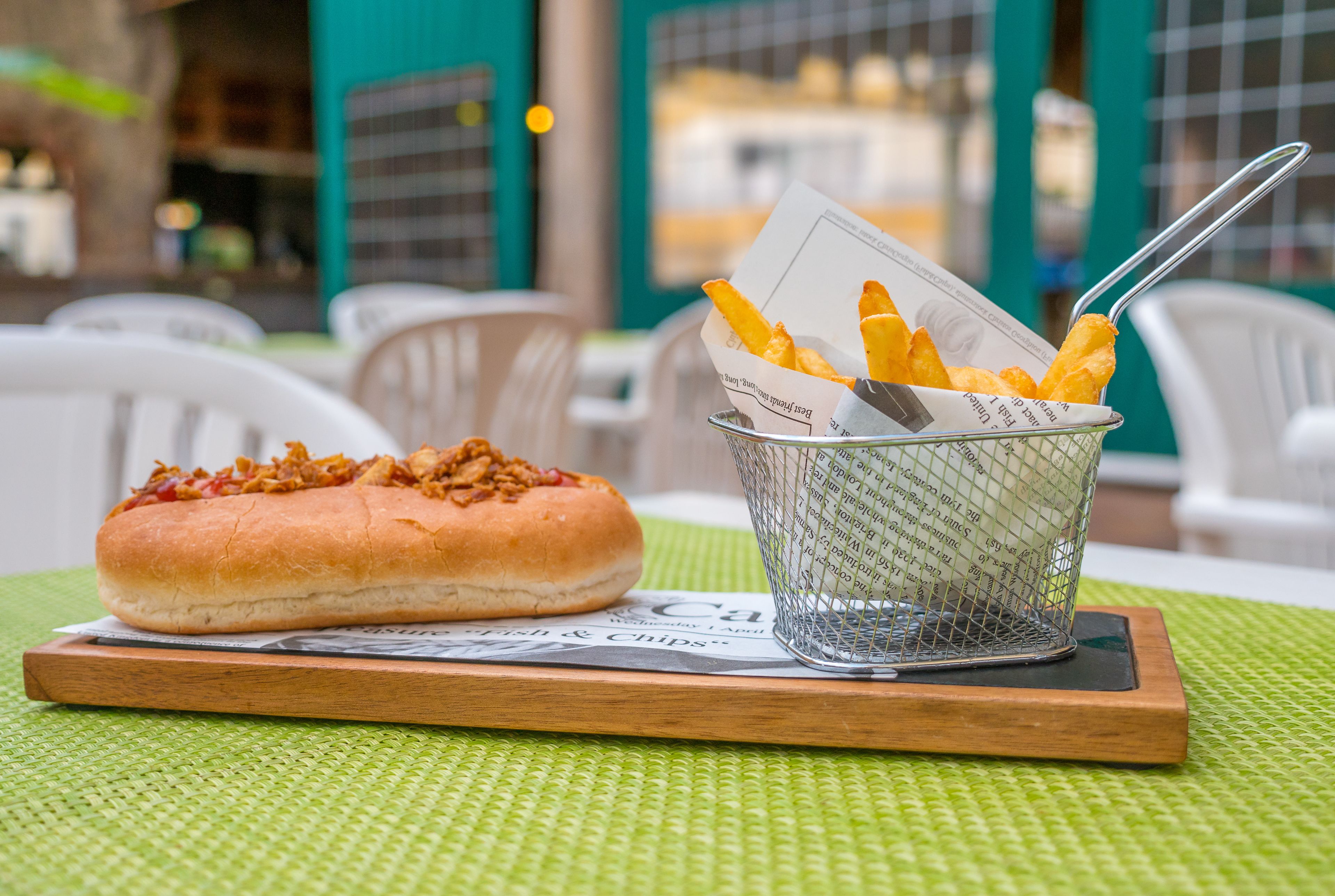 A meal with a bun and fries on a wooden board, placed on a green mat.