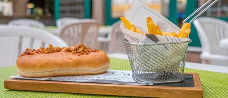 A meal with a bun and fries on a wooden board, placed on a green mat.
