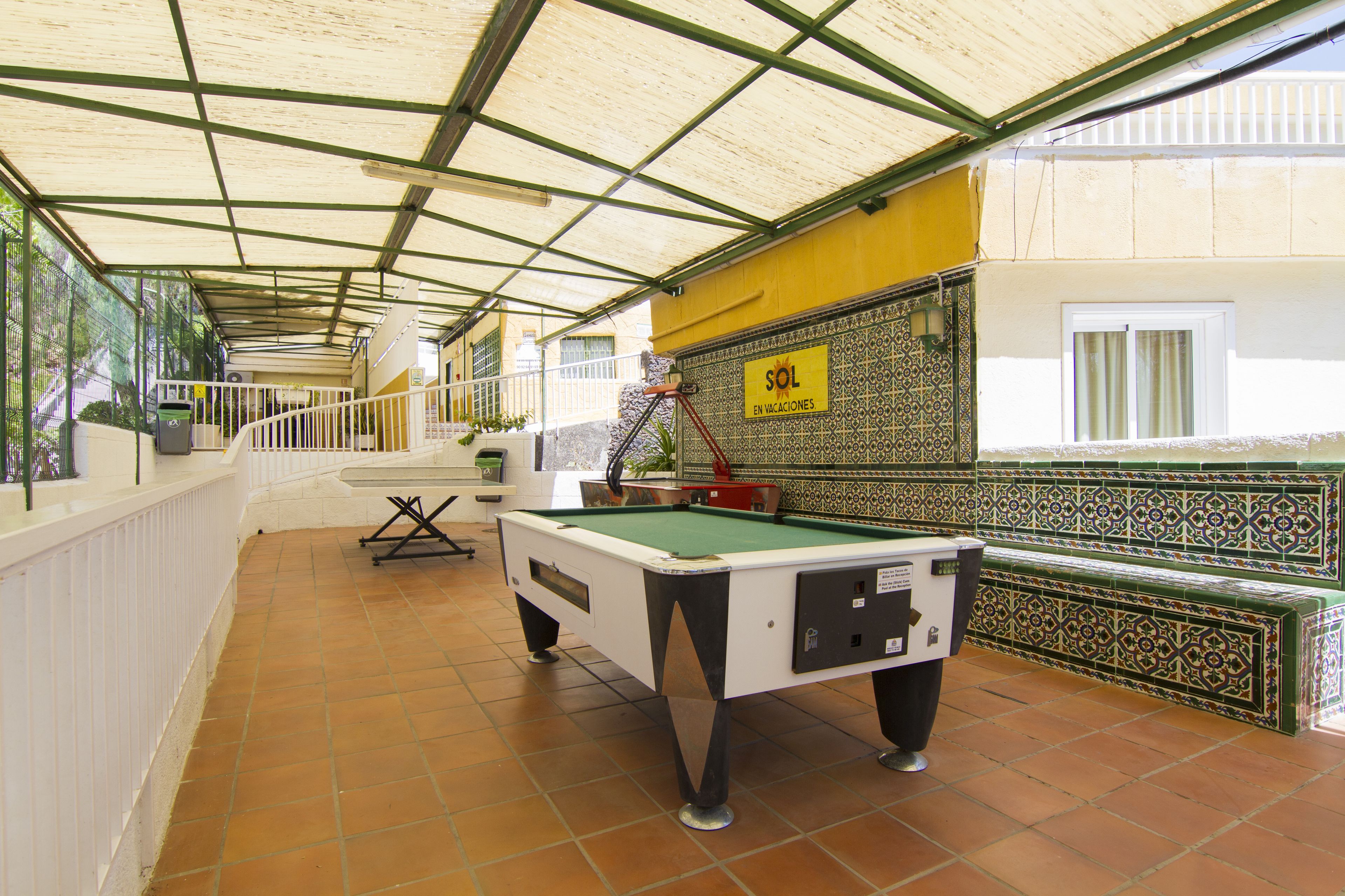 Une table de billard se trouve dans un espace abrité, doté d’un sol carrelé, d’une rambarde et d’un mur recouvert de carreaux décoratifs.
