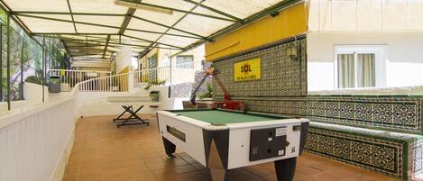 A pool table in a covered area with a tiled floor, a railing, and a wall with patterned tiles.