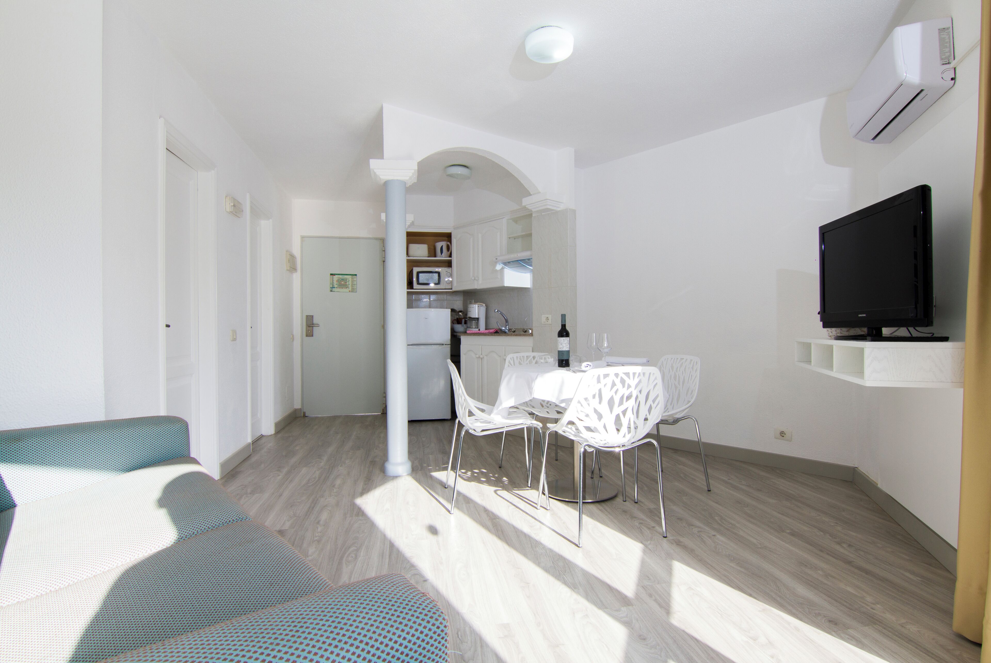 Ein modernes Wohnzimmer mit Sofa, Esstisch und Stühlen, einer Küchenzeile mit Geräten sowie einem Wand-Fernseher.