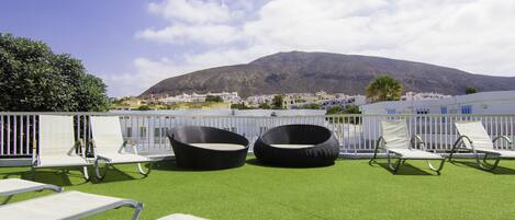 A rooftop terrace with outdoor seating and a view of a mountain.