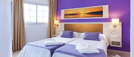 A hotel room with two beds, purple walls, a sunset painting, and a window with curtains.