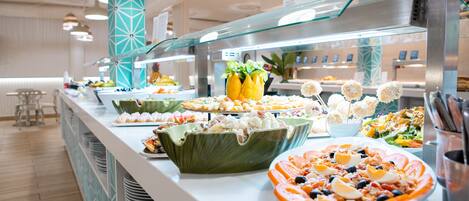 A buffet with various food items and a seating area in the background.