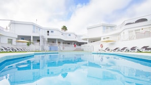 A swimming pool surrounded by white buildings with balconies, a palm tree, and a lifebuoy. - Checkin Bungalows Atlantida (Arona)