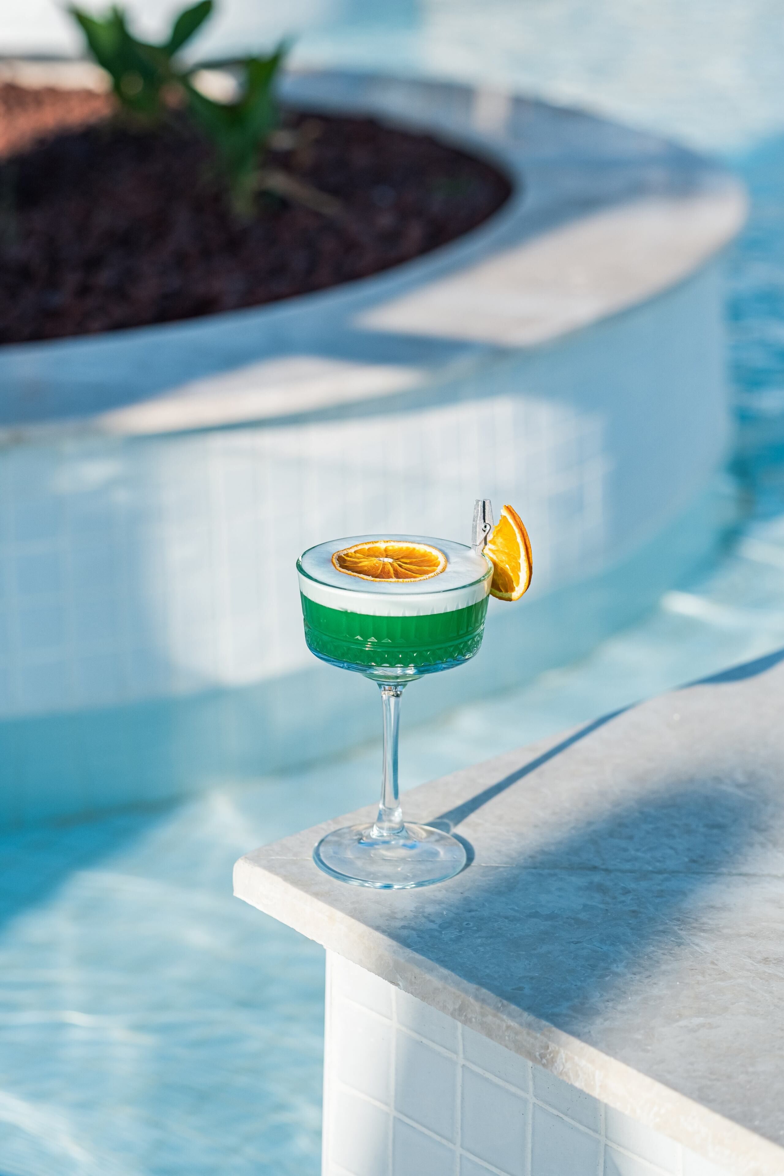 Ein Cocktailglas mit Orangenscheibe auf einem Beckenrand.