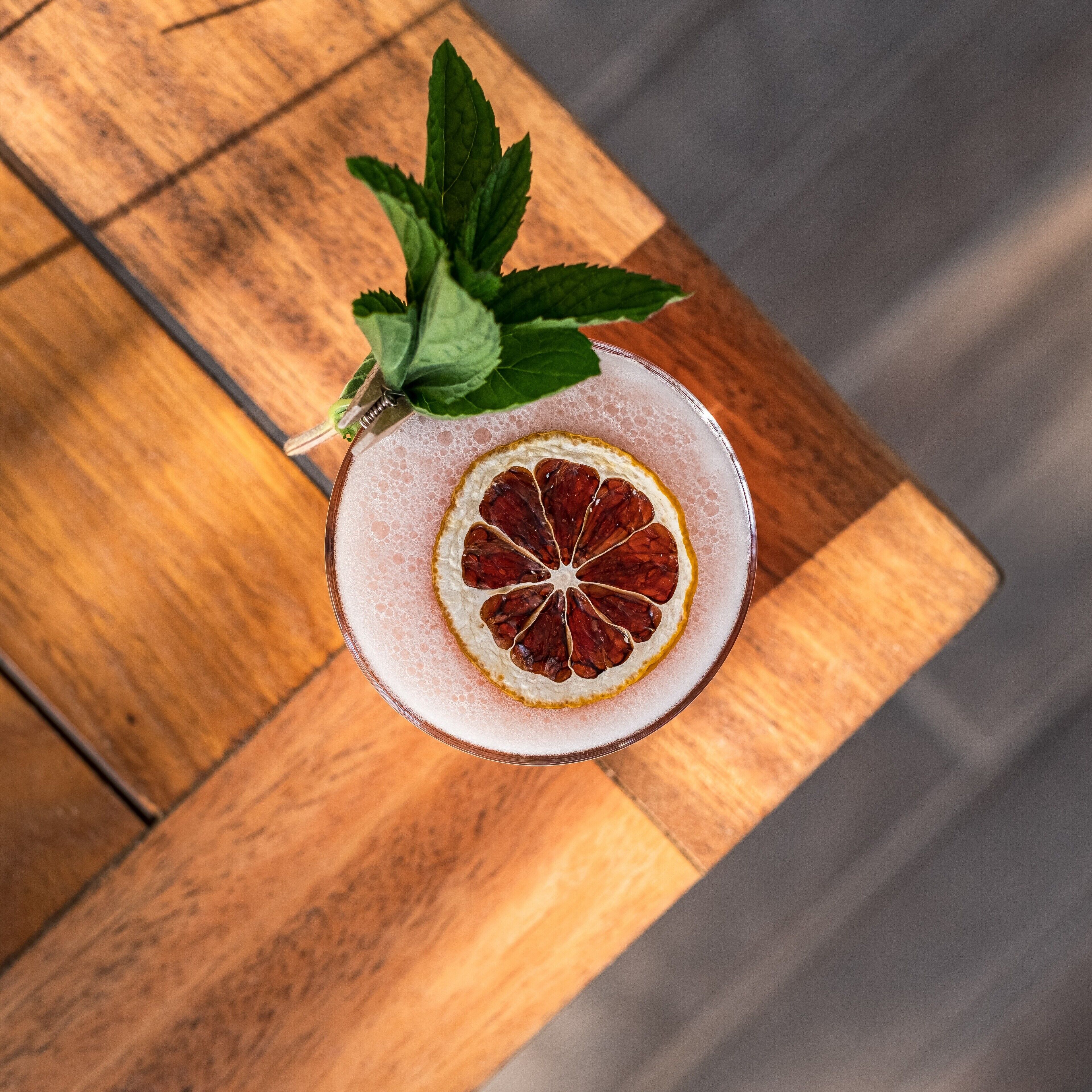 A cocktail with a slice of blood orange and mint leaves on a wooden table.