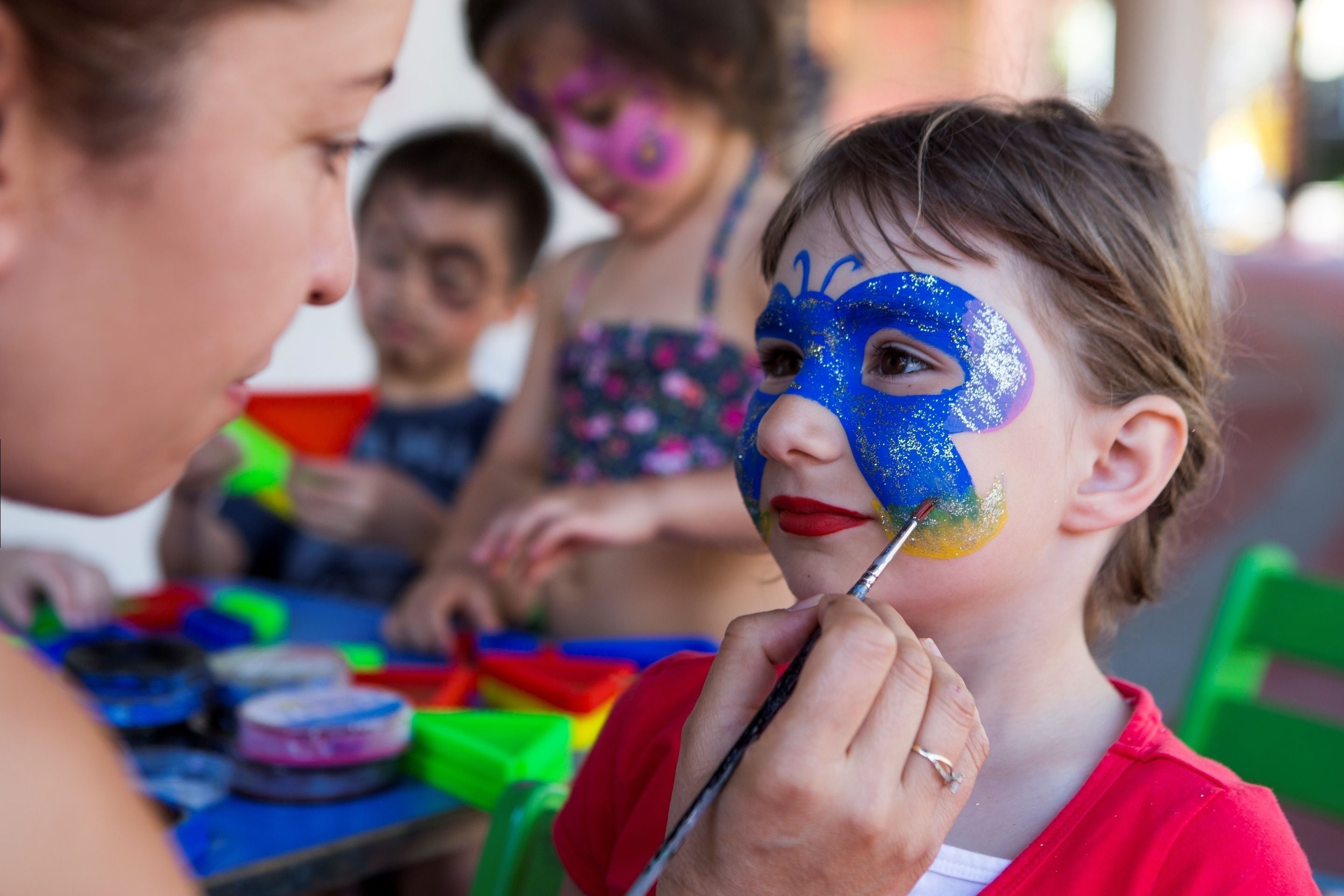 Une personne est en train de peindre le visage d  ’un enfant avec de la peinture bleue et jaune.