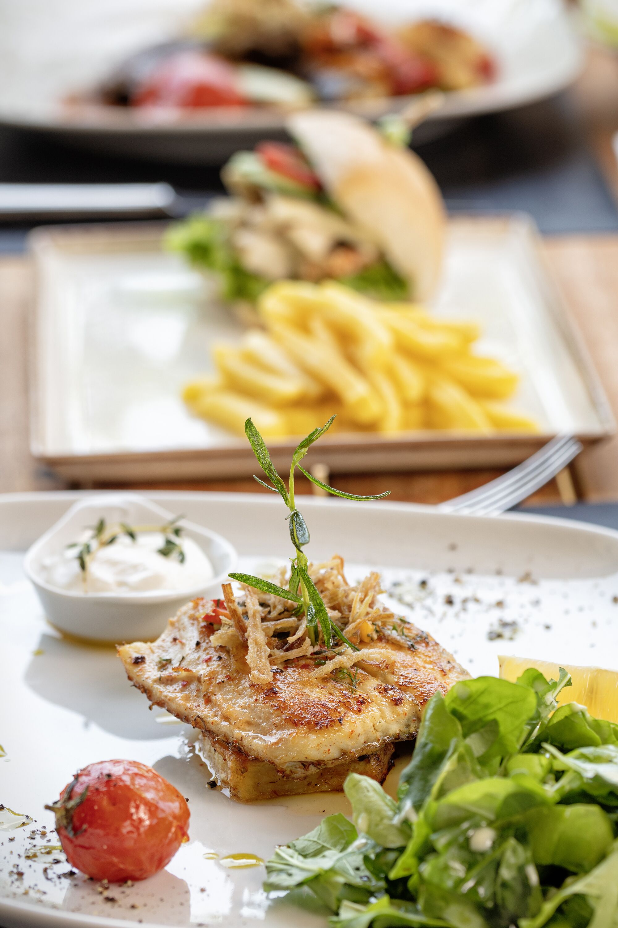 A plate of food with a piece of grilled fish, a side of fries, a small bowl of sauce, and a cherry tomato.