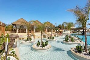 A resort pool area with multiple water features, palm trees, and thatched-roof structures. - Liberty Hotels Lara - All Inclusive (Antalya)