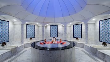 Ein luxuriöses Badezimmer mit einem runden Waschtisch in der Mitte, Marmorwänden und dekorativen Fliesen.