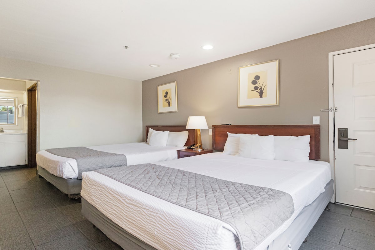 A hotel room with two beds, a bathroom, and a door.