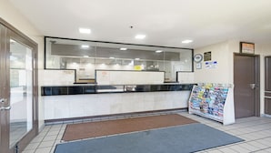 Un espace d’accueil avec un comptoir d’enregistrement, un panneau d’affichage où sont accrochées des prospectus, et une porte située sur la gauche.