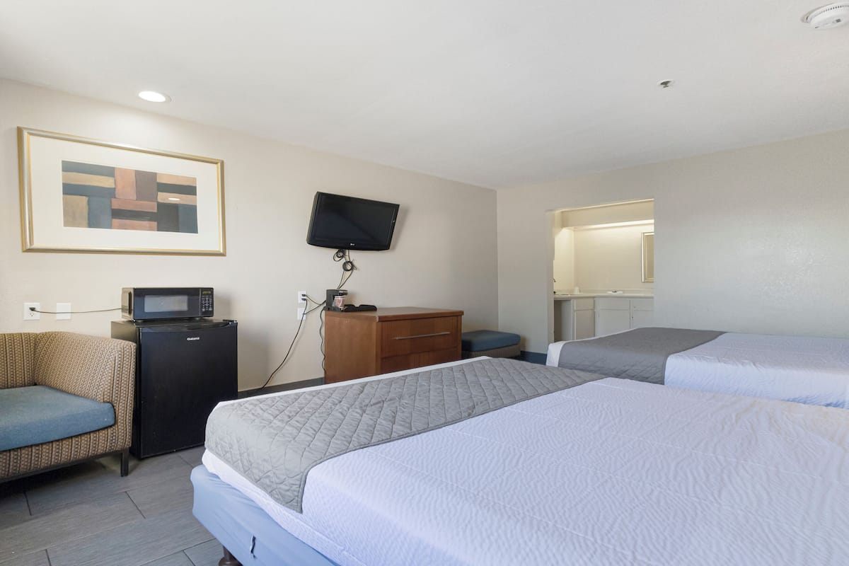 A hotel room with two beds, a sofa, a television, a microwave, and a desk.