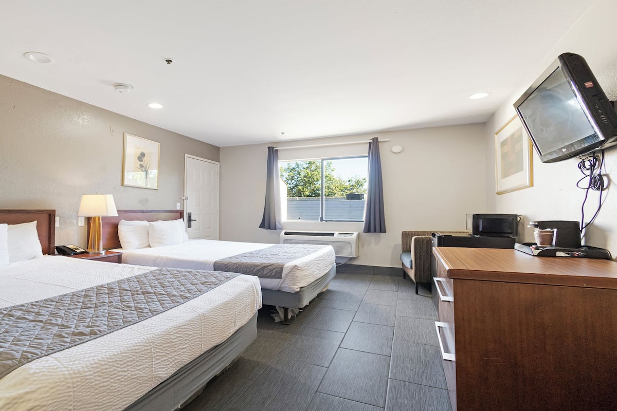 A hotel room with two beds, a desk with a computer, a TV, and a window with curtains.