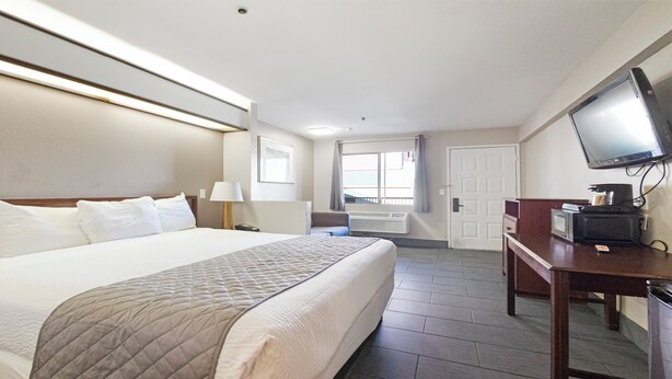 Une chambre d’hôtel avec un grand lit, un bureau avec une télévision, une fenêtre et une porte.