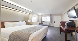 Habitación de hotel con una cama grande, un escritorio con televisor, una ventana y una puerta.