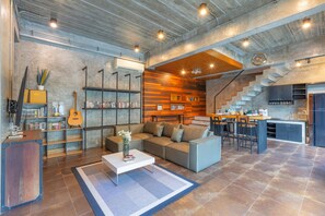 A modern living space with a sofa, coffee table, bookshelves, a guitar, and a kitchen area with a staircase.
