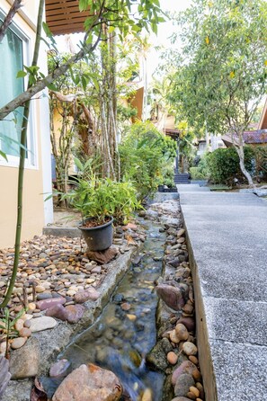 A garden with a small stream, potted plants, and a concrete pathway. - Aonang Paradise Resort (Krabi)