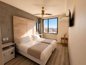 A modern hotel room with a large bed, a ceiling fan, a TV, and a city view. - Hotel Internacional (Mendoza)