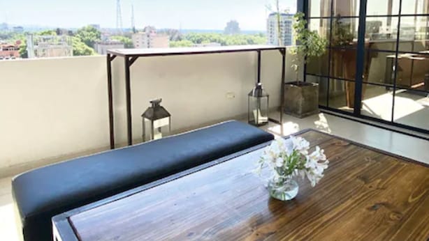 A balcony with a wooden table, a bench, and a vase of flowers. - Hotel Internacional (Mendoza)