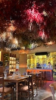 En restaurantindretning med dækketøjet borde, et barområde og en dekorativ loftskonstruktion.