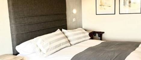 A neatly made bed with a grey headboard, white bedding, and a grey throw blanket. There are two framed artworks on the wall above the bed.