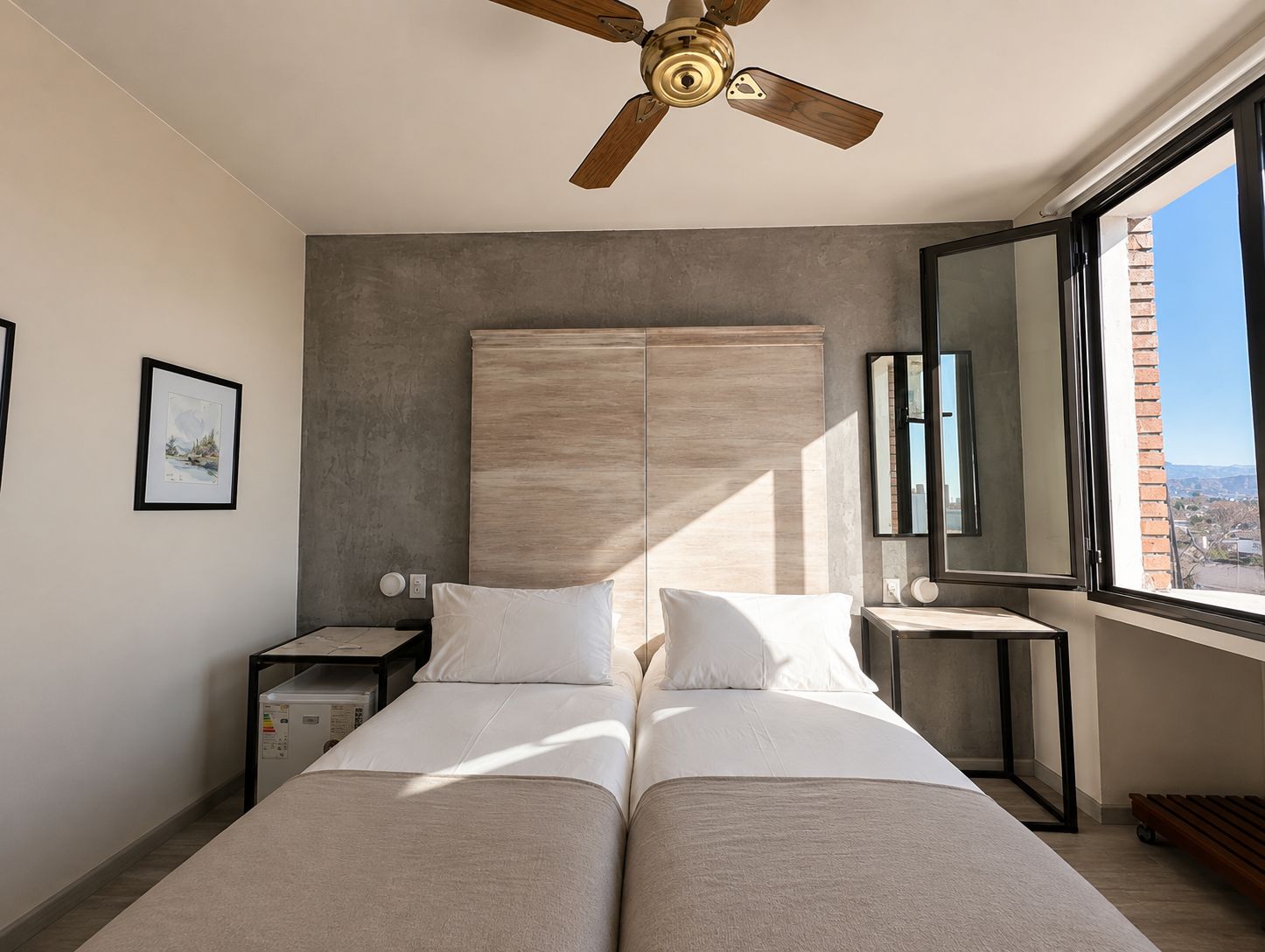 Un dormitorio con cama, ventilador de techo, mesita de noche y una ventana con vistas, además de un cuadro en la pared.