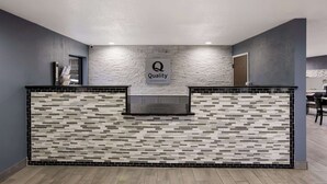 Un espace d’accueil au design moderne, avec un mur à texture particulière et un logo sur lequel on peut lire : « Qualité, garantie par Choice Hotels ».