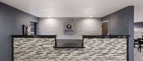 Un área de recepción de diseño moderno, con una pared texturizada y un logotipo que dice "Quality by Choice Hotels".