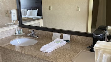 Un bagno d'albergo con uno specchio grande, due lavandini, un asciugacapelli e una macchina per il caffè.