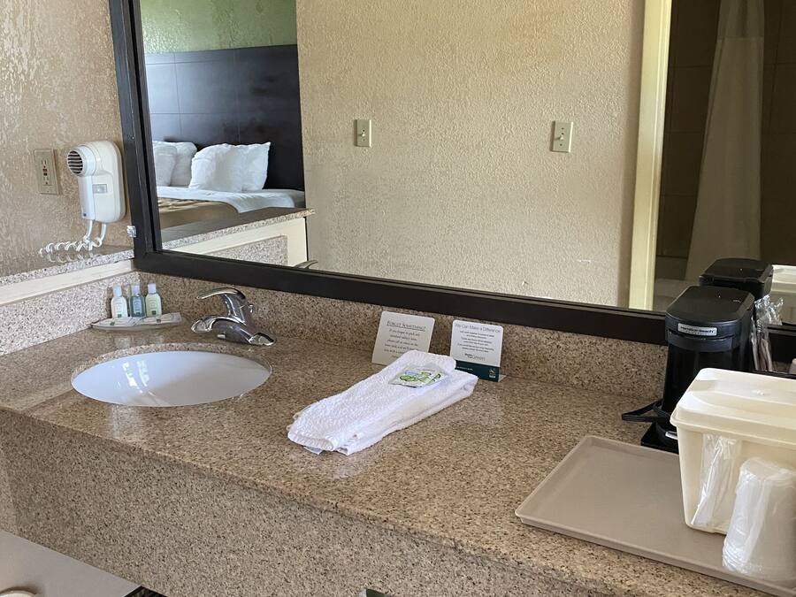 Een hotelbadkamer met een grote spiegel, twee wastafels, een haardroger en een koffiezetapparaat.