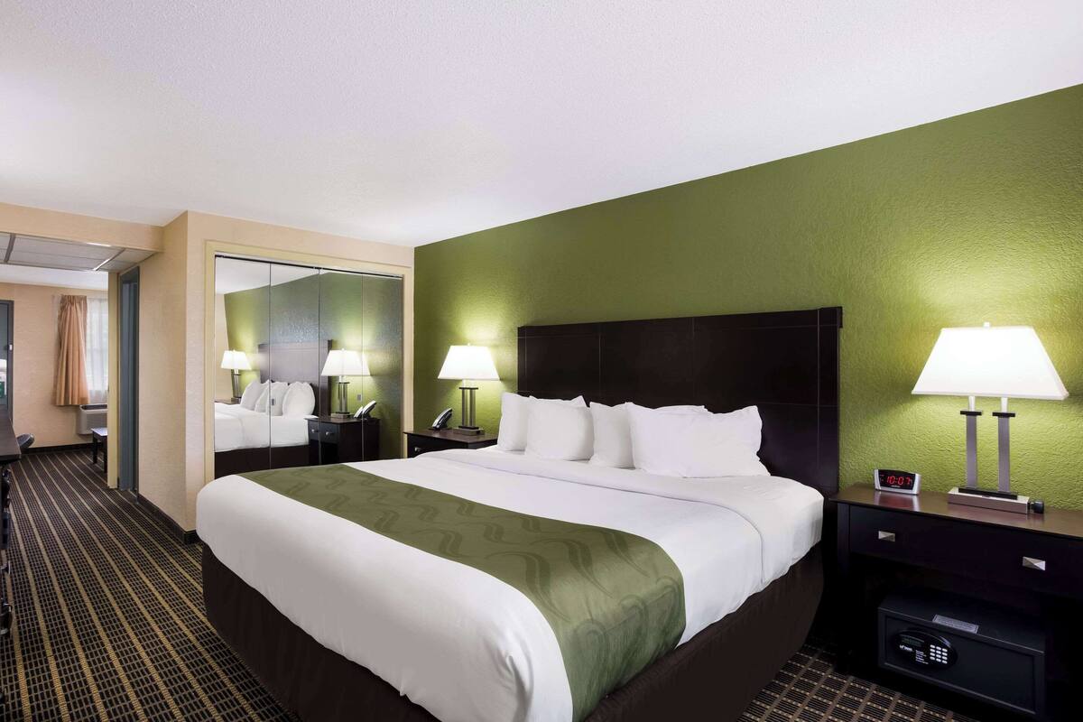 A hotel room with a large bed, green walls, two bedside lamps, a nightstand with a phone, and a mirror.