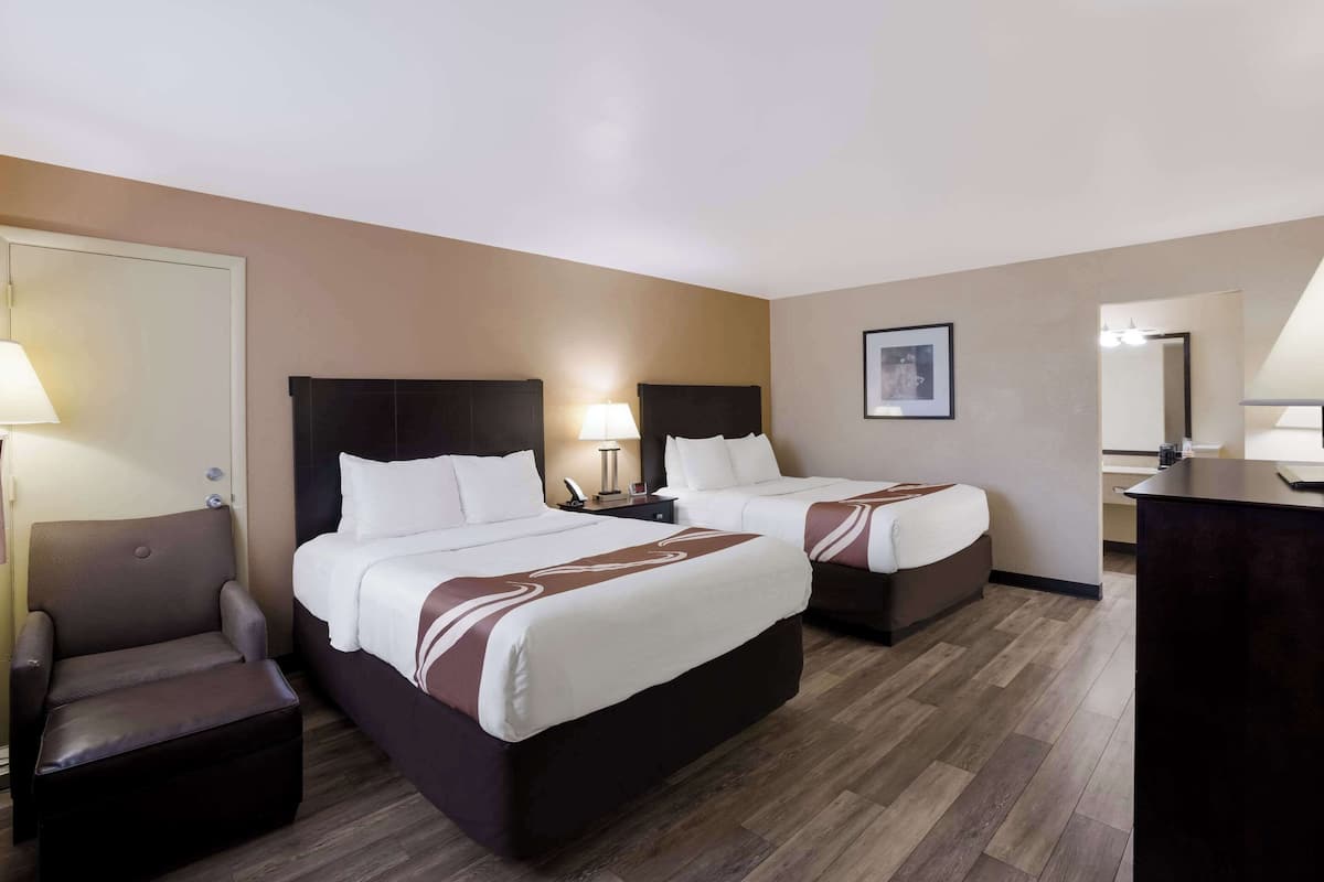 A hotel room with two beds, a chair, a desk, and a mirror.