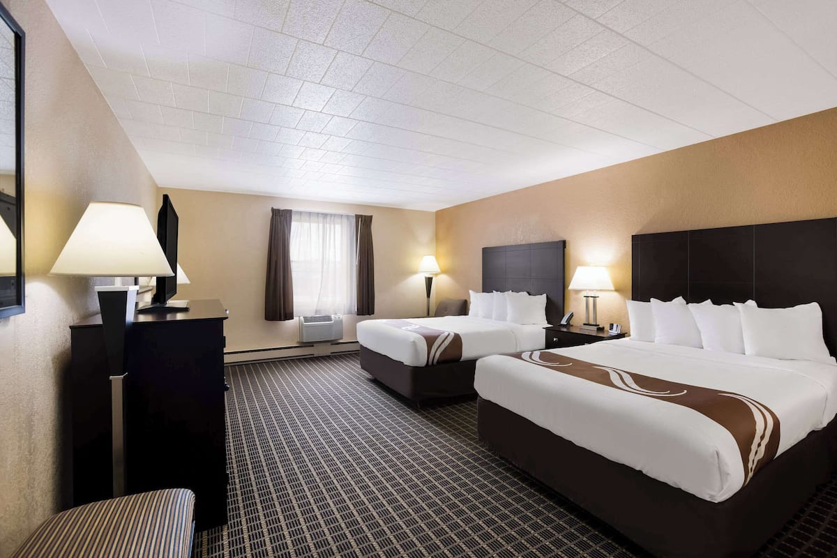 A hotel room with two beds, a desk, a chair, and a large window with curtains.