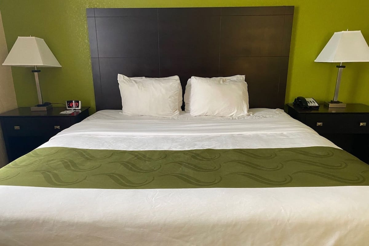 A hotel room with a large bed, two bedside tables, a nightstand, a lamp, and a clock.