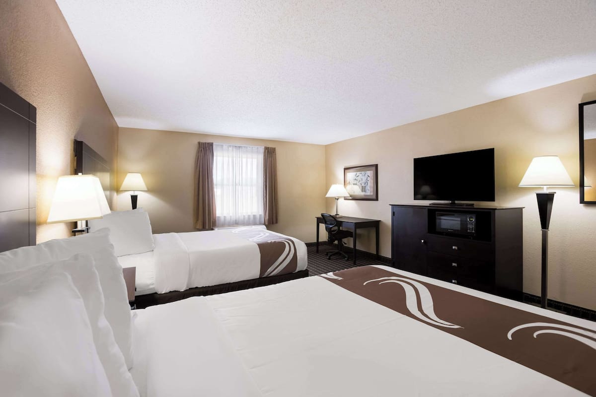 A hotel room with two beds, a desk, a television, and a minibar.