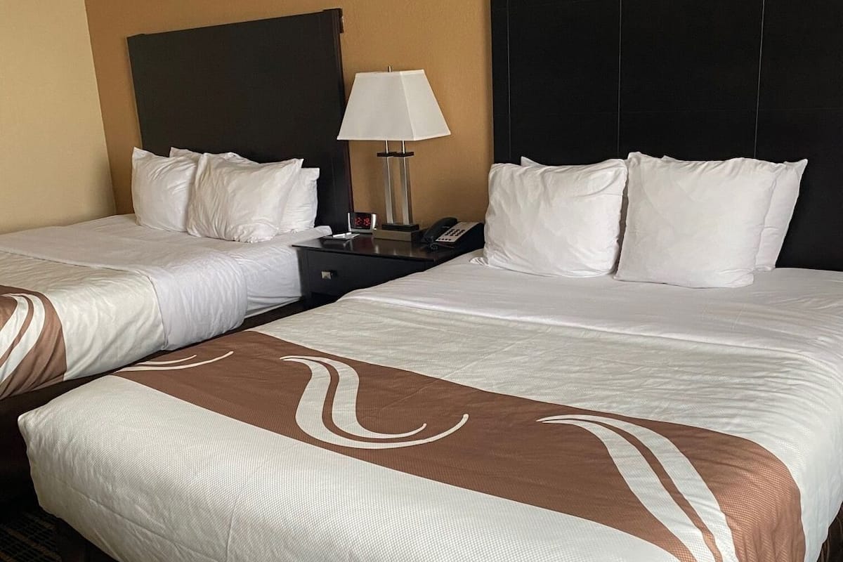 A hotel room with two beds, a nightstand with a lamp, and a clock.
